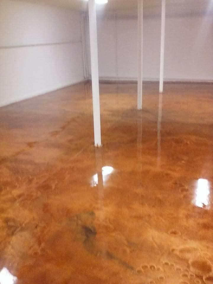 Polished brown epoxy floor in a white-walled room with support pillars; reflections and light.