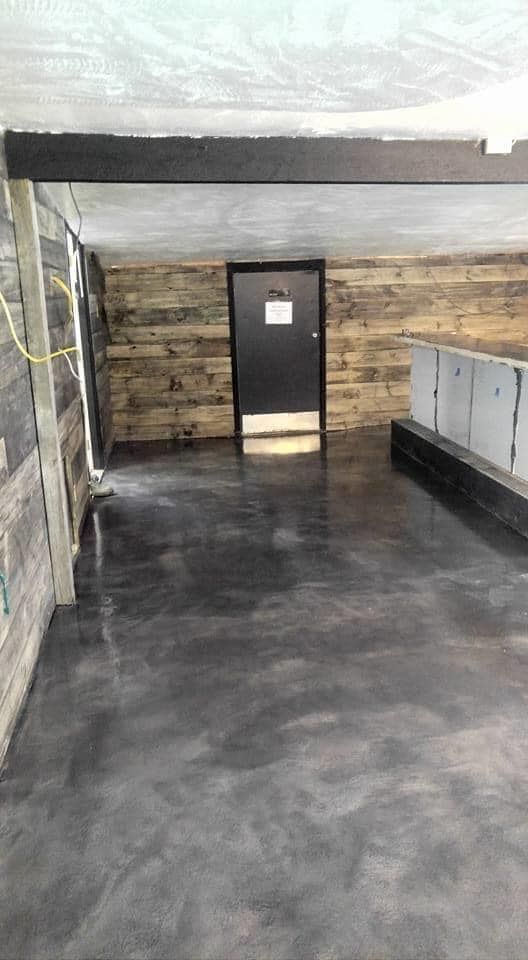 Interior with dark gray floor, wood paneling, black door, and exposed ceiling beams.