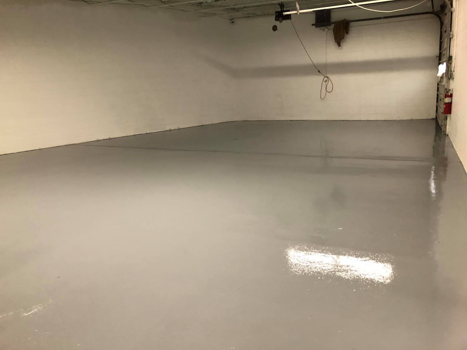 Empty room with gray epoxy floor and white walls. A fire extinguisher is visible.