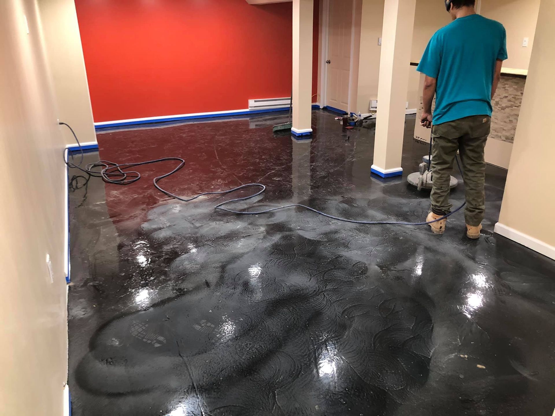 Person works on a black epoxy floor. Room has red wall, blue tape, and beige columns.