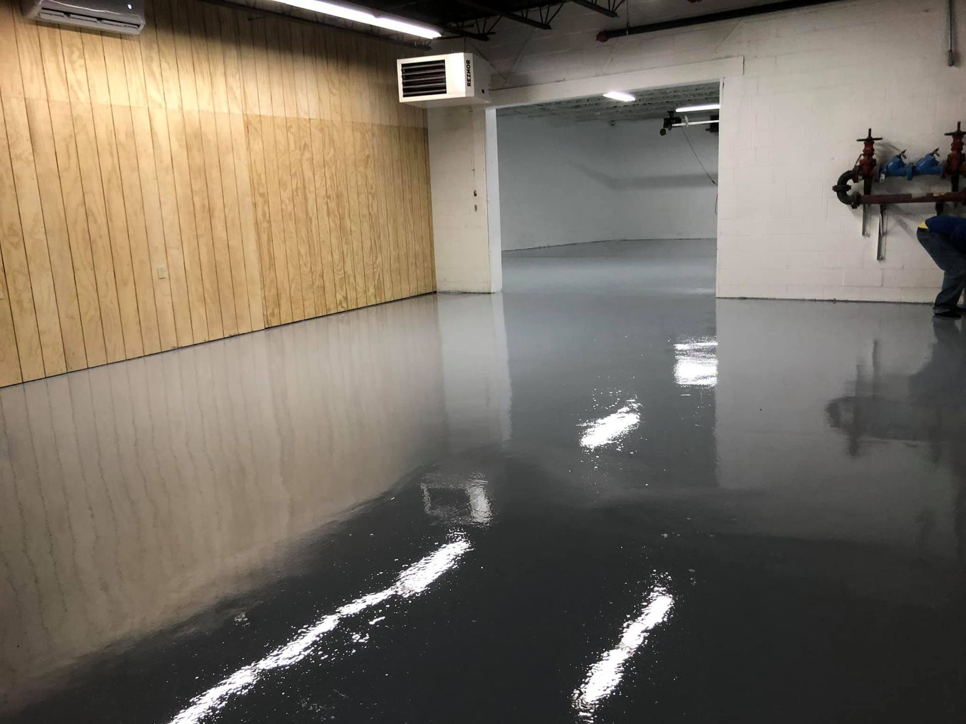 A room with a gray, glossy floor, wooden wall, and open doorway to another room.