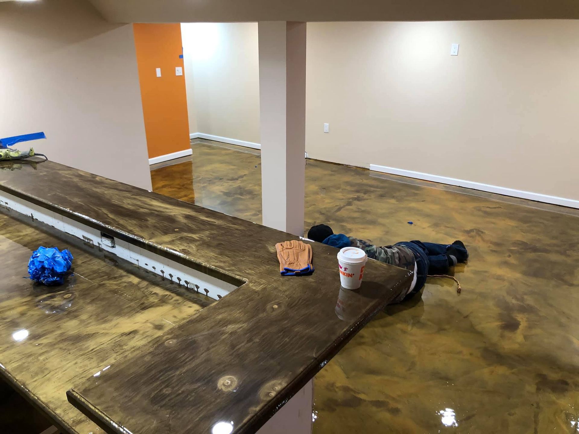Finished basement with a bar, gold-toned epoxy floor. Person is lying on the floor with a coffee cup.