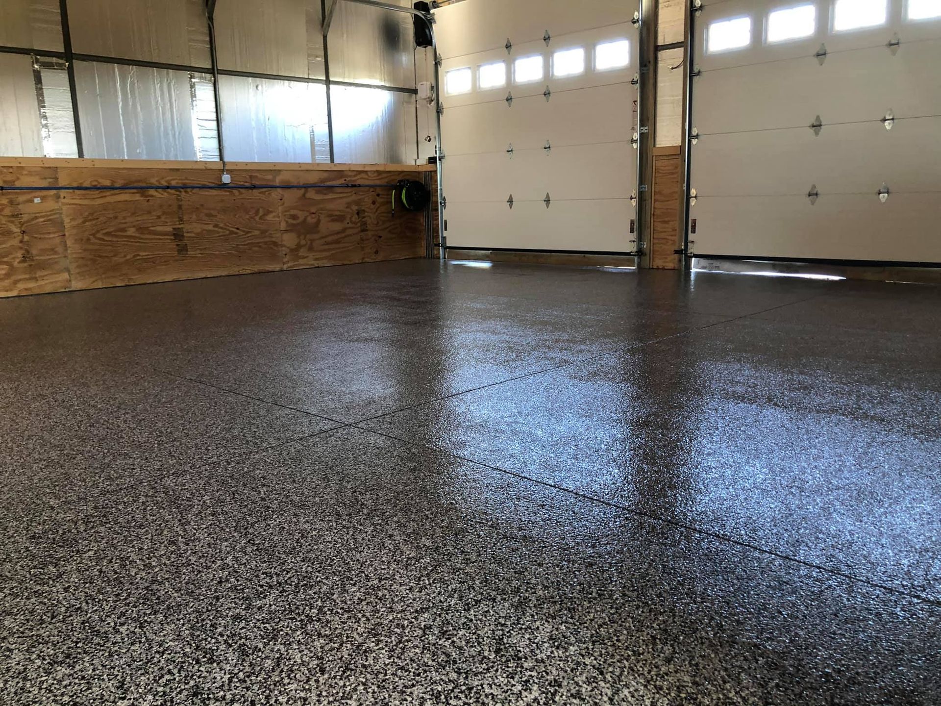 Epoxy coated floor in a garage with two closed white garage doors.