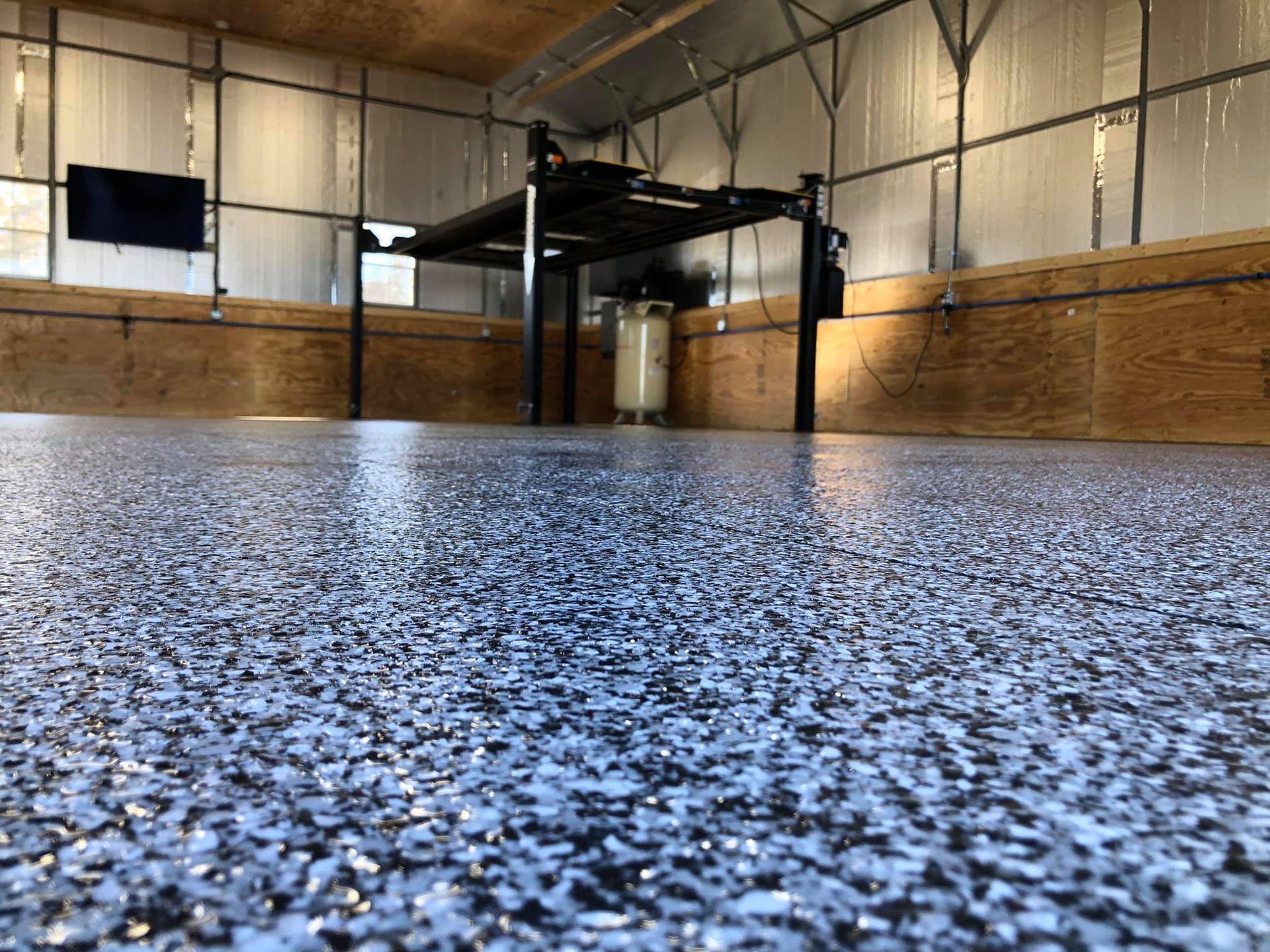 Epoxy-coated garage floor with a car lift, wood paneling, and a mounted TV.