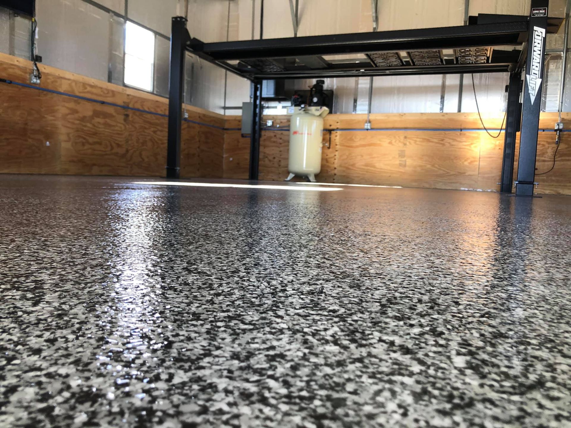 Shiny, speckled gray and black epoxy garage floor; car lift; air compressor; wood panel walls.