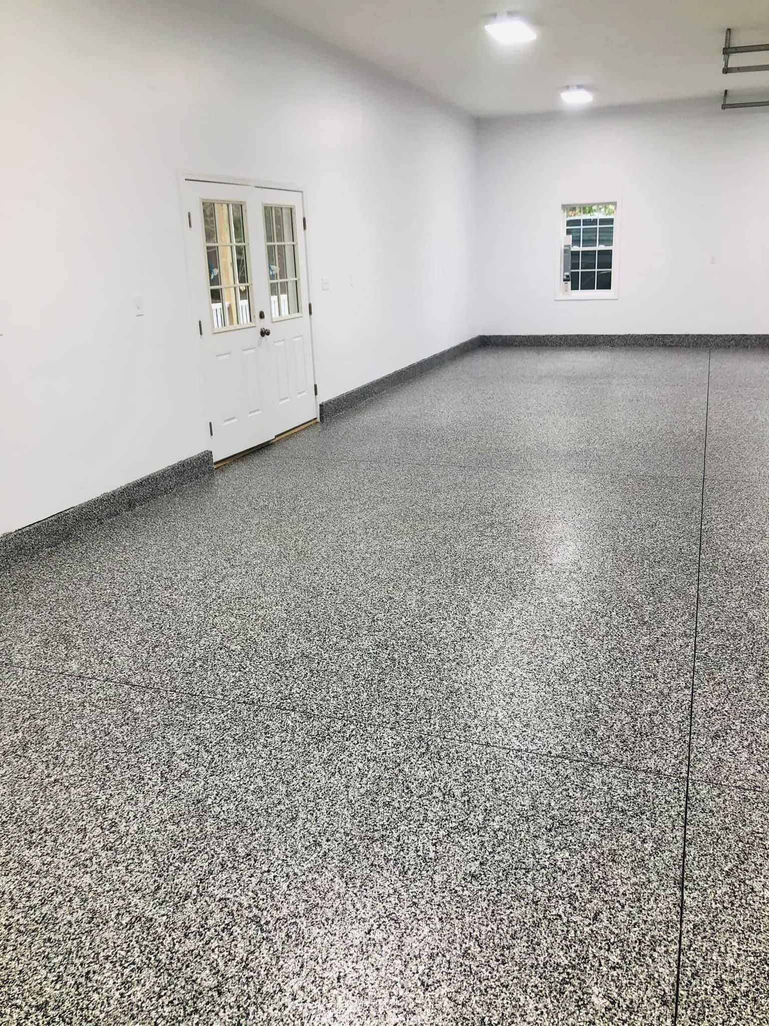 White garage with epoxy flooring in speckled gray and white, white walls, double doors, and a window.