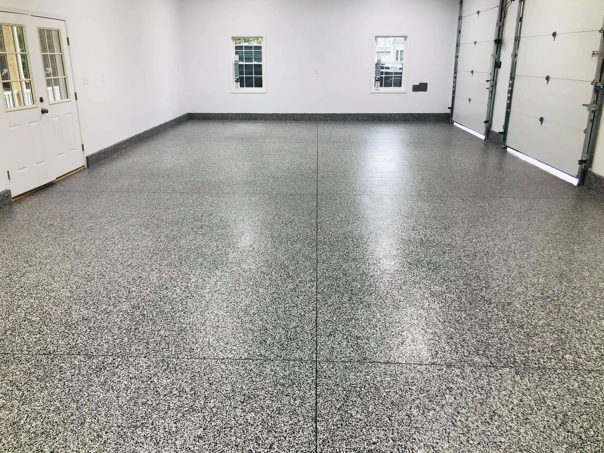 Finished garage with speckled gray epoxy floor, white walls, and garage doors. Two windows visible.