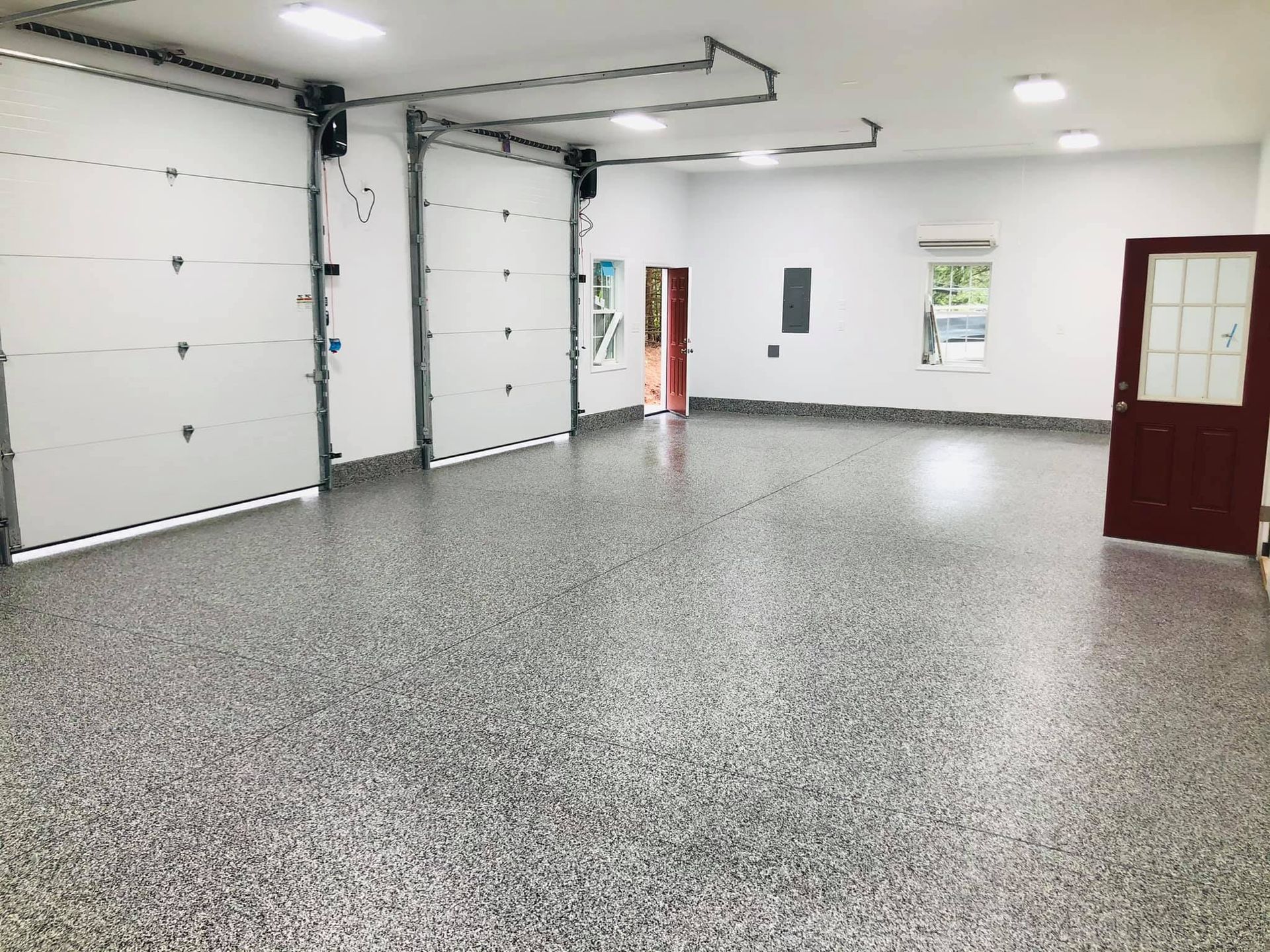 Spacious, newly built garage with epoxy flooring, white walls, two overhead doors, and a red door.