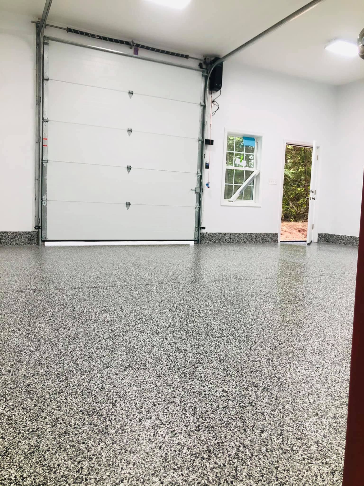Garage interior with speckled gray floor, white walls, closed garage door, window, and a door.
