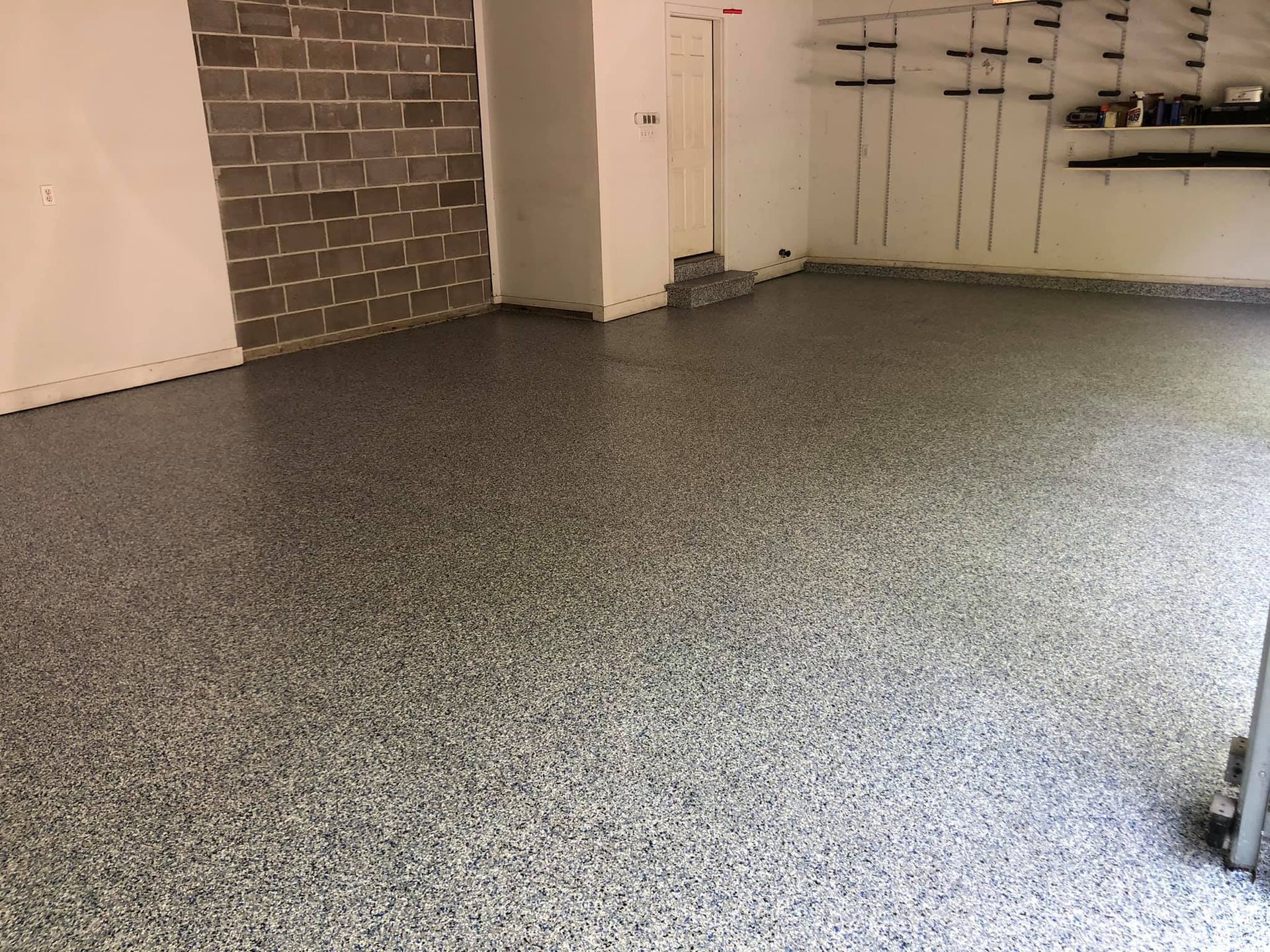 Garage with a speckled gray epoxy floor, brick wall, and white walls.