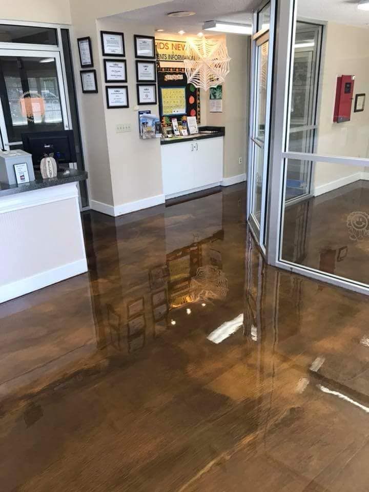 Shiny brown epoxy floor in an office lobby with glass doors and a reception desk.