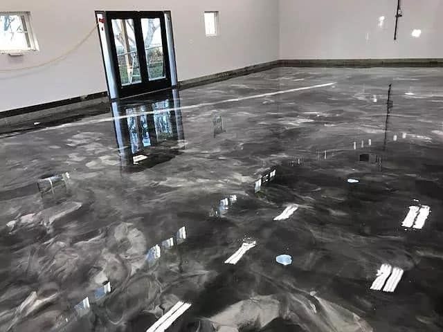 Glossy, metallic gray epoxy garage floor reflecting a black door and sunlight.