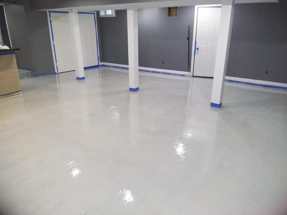 Basement with glossy white epoxy floor. Gray walls, white support beams and trim. Blue painter's tape visible.