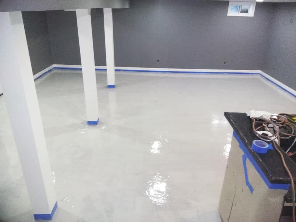 Basement with freshly painted light gray floor, blue tape, white support columns, and gray walls.