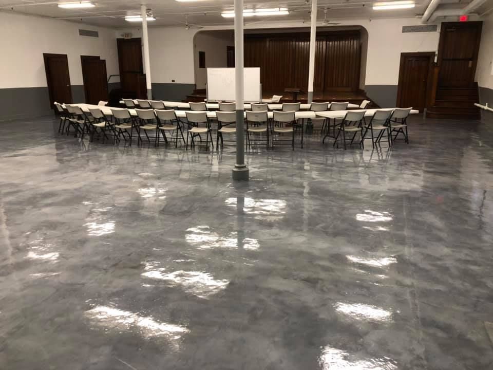 Shiny, gray epoxy floor in large room with tables, chairs, and pillars.
