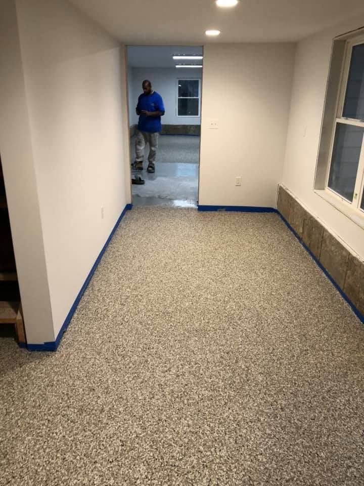 Room with speckled flooring, white walls, and a person standing in the doorway.