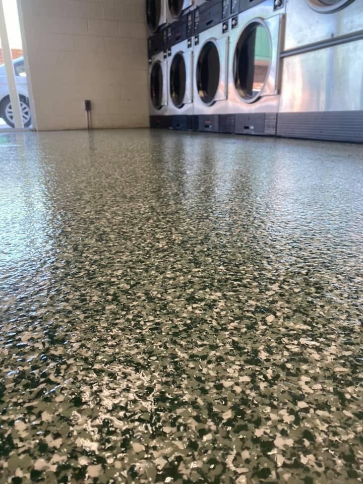 Epoxy-coated floor in a laundromat, speckled with green, white, and gray flakes, with several washing machines in the background.