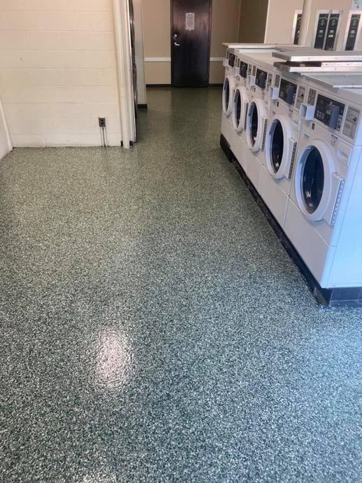 Laundry room with a row of washing machines and speckled green flooring.