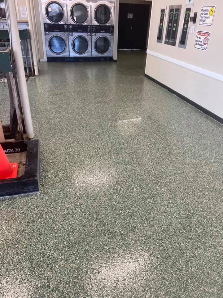 Laundry room with green flecked floor, washing machines in the background, and a traffic cone on the left.