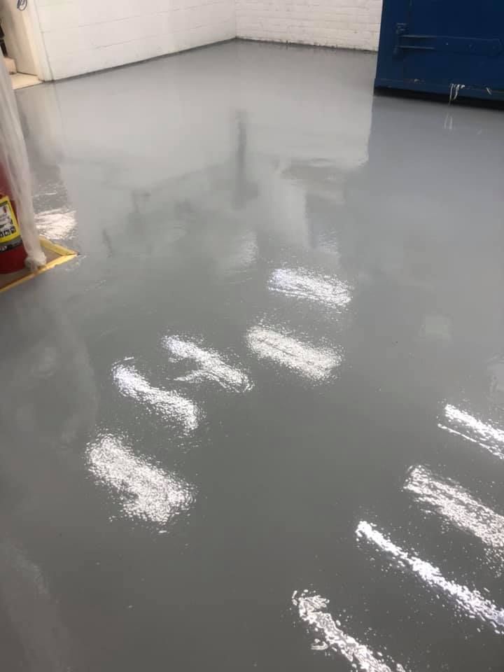 Grey, glossy epoxy floor in a room, reflecting overhead lights, creating bright highlights.