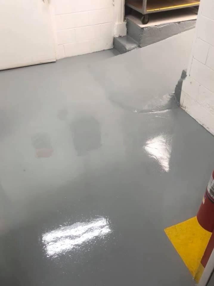 Gray, reflective floor in a commercial kitchen with a yellow marking.