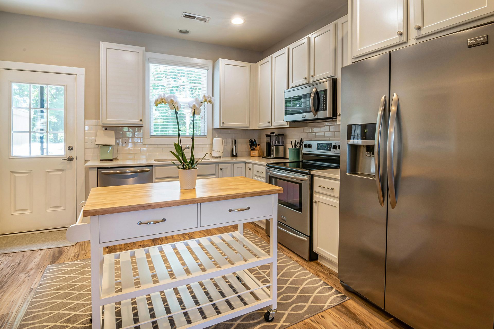 Bright kitchen with white cabinets, stainless steel appliances, and a butcher-block island on a rug.