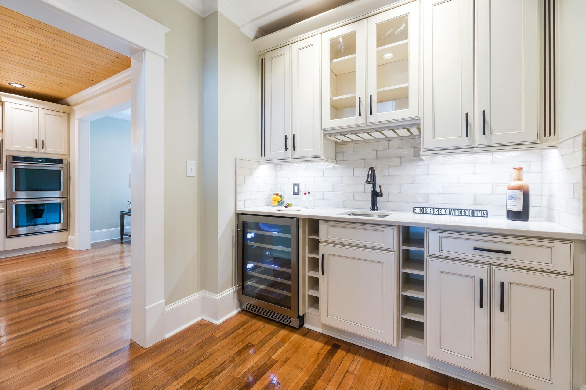 Creamy-white built-in bar area with wine fridge, sink, cabinets, and wine glass rack.