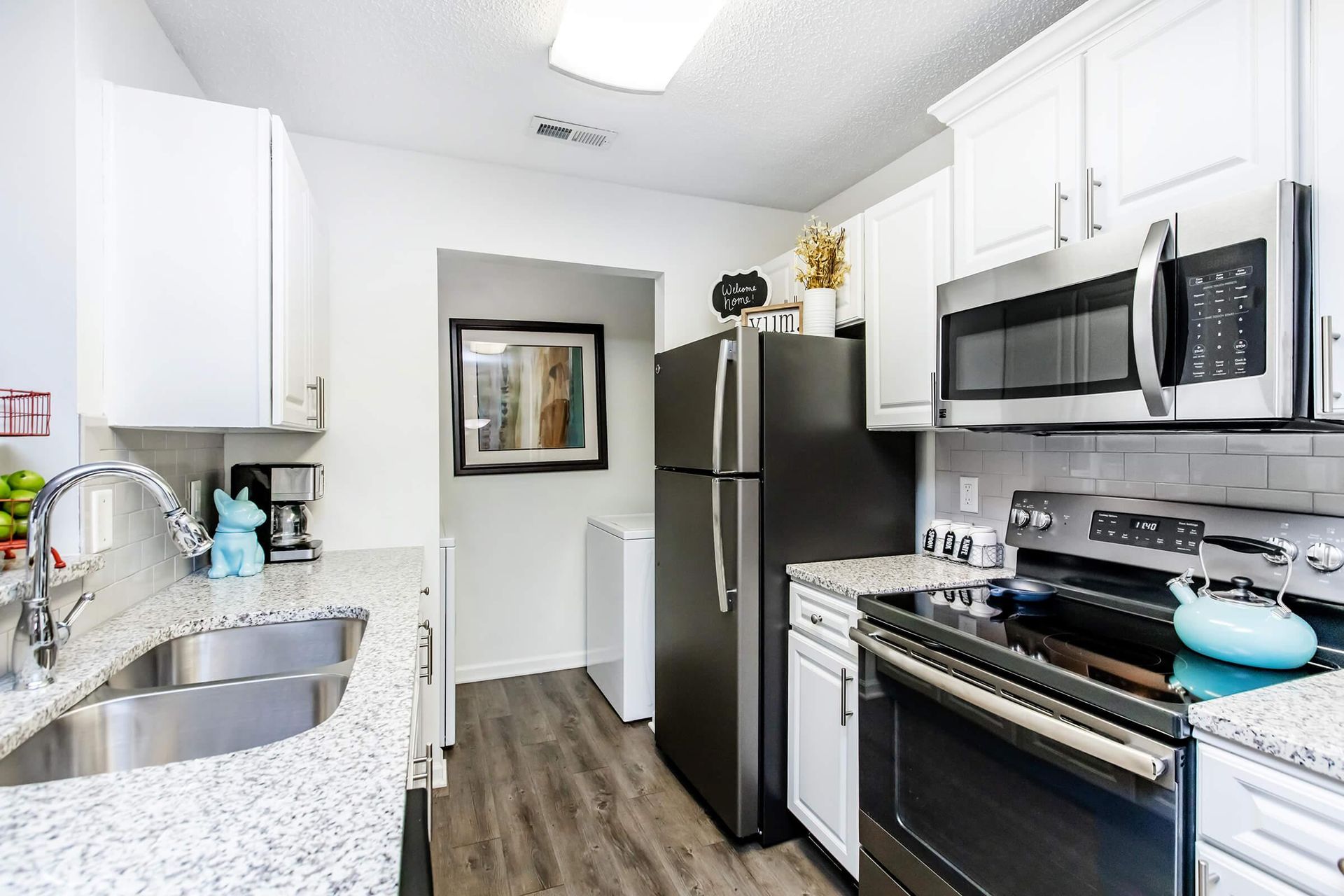 A bright kitchen with white cabinets, granite countertops, stainless steel appliances, and a black refrigerator.