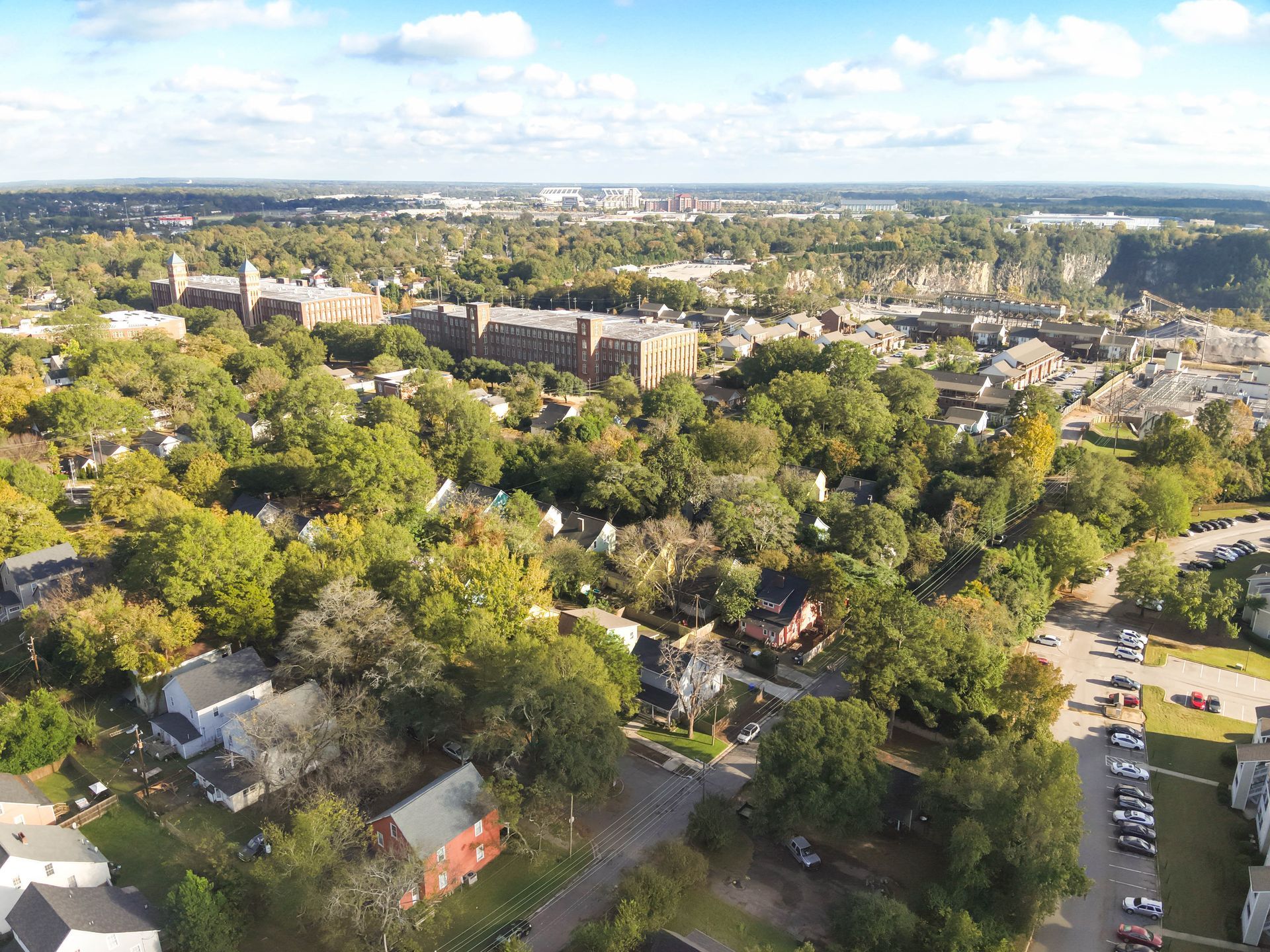 Aerial view of a town with buildings, trees, and roads, blue sky above.