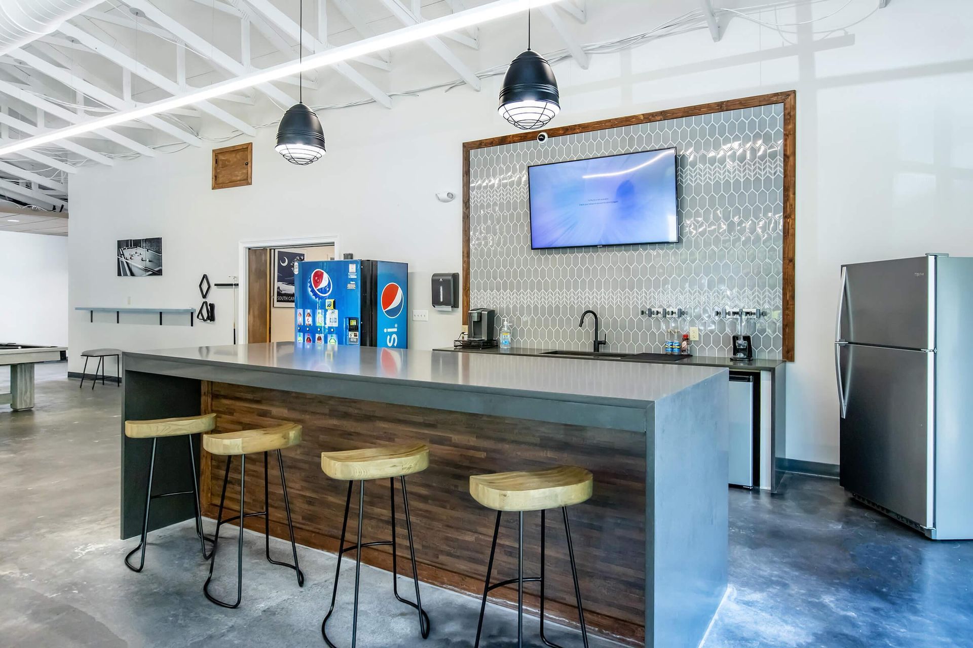 Modern break room with counter seating, soda dispensers, and a TV.