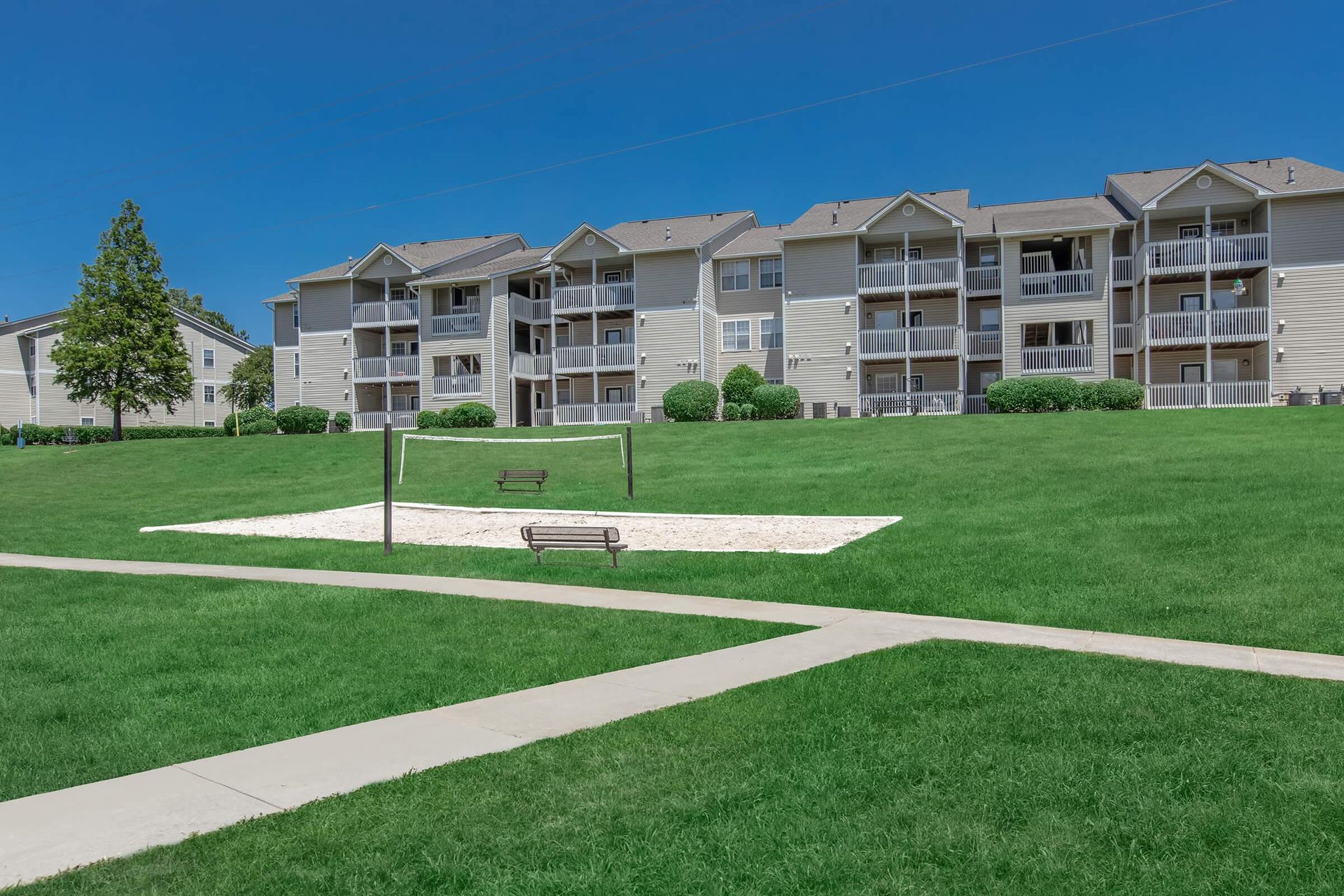 Apartment complex with a volleyball court on a grassy lawn under a blue sky.