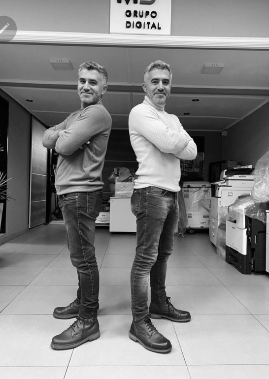 Dos hombres, espalda contra espalda, con los brazos cruzados.