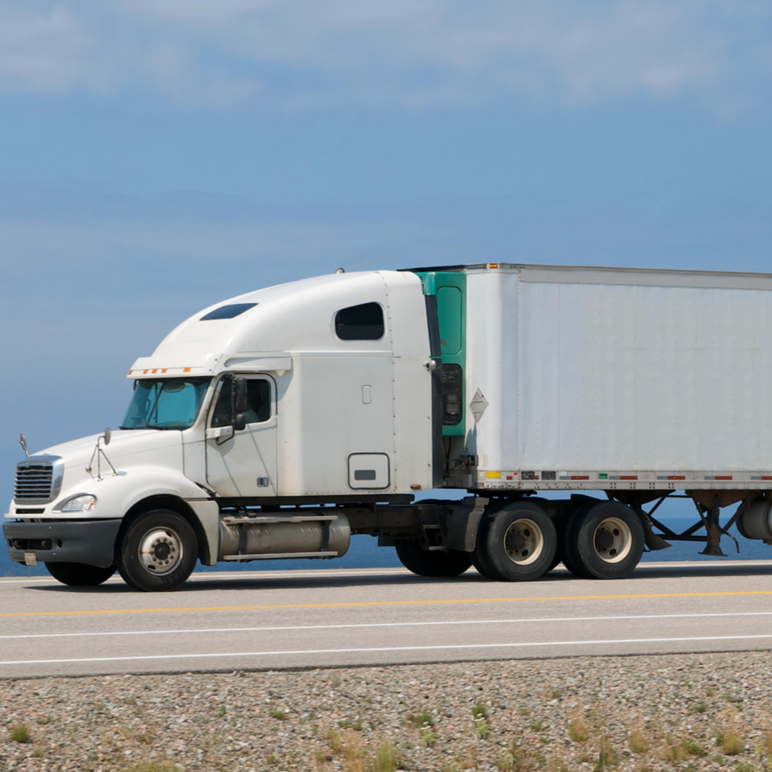 A white semi truck with a green trailer is driving down a road.
