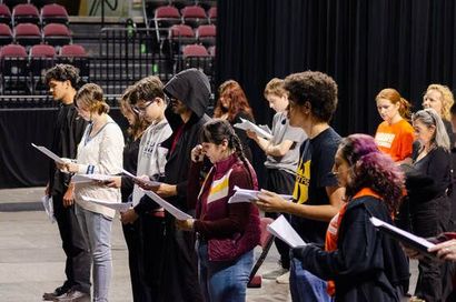 A group of people standing on a stage, reading from scripts held in their hands.
