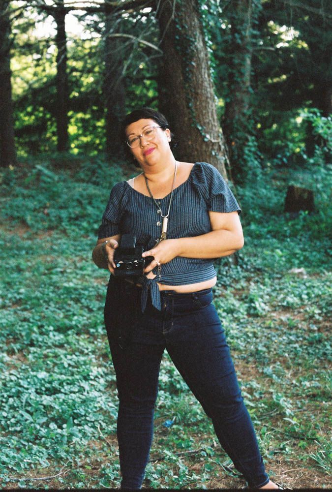 A person with a beard and glasses wearing a striped button-down shirt, smiling warmly indoors.