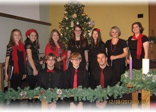 A group poses in front of a Christmas tree, wearing black outfits with red accents, in a room decorated for the holidays.