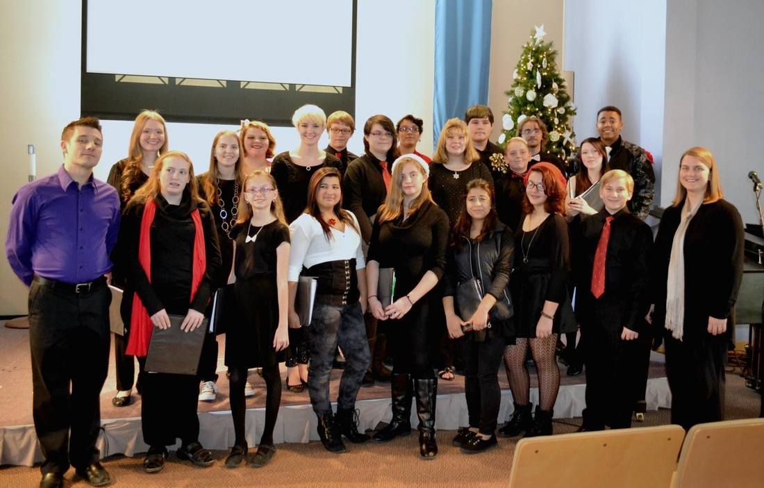 A group of people standing on a stage in front of a Christmas tree for a performance.