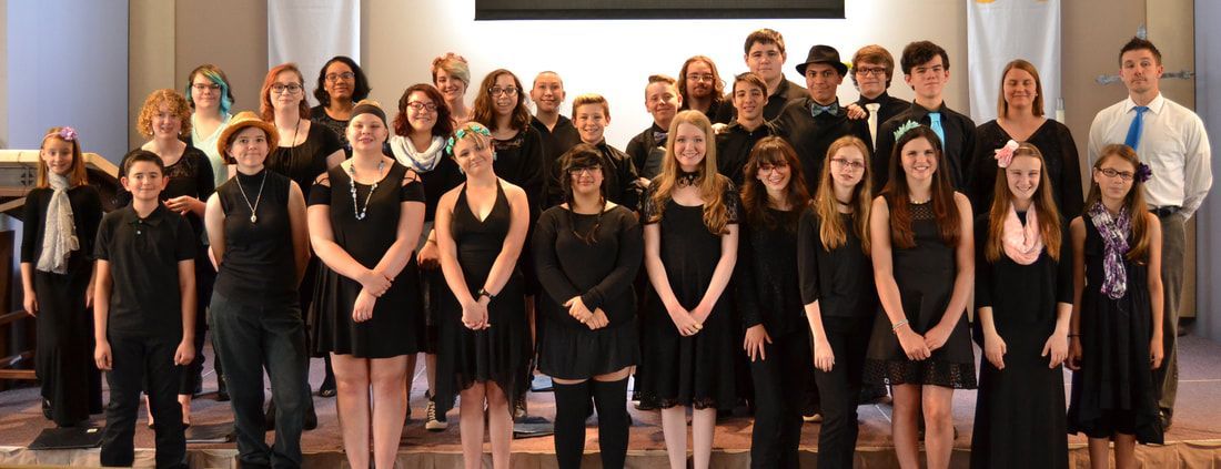 A group of people wearing black formal attire poses for a photo on a stage in front of a white wall.