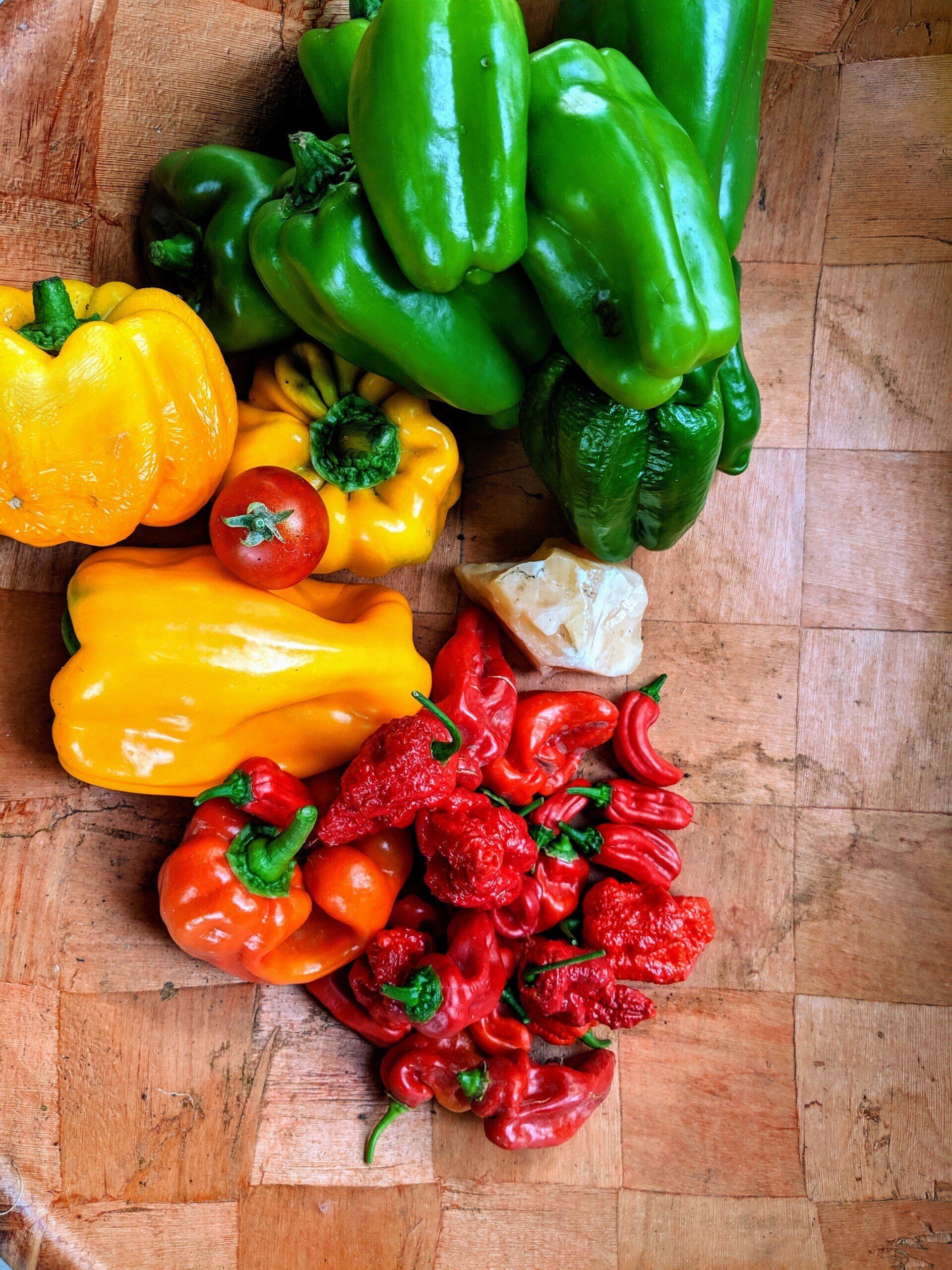 Colorful assortment of bell peppers and hot peppers on a wooden surface, including green, yellow, orange and red.