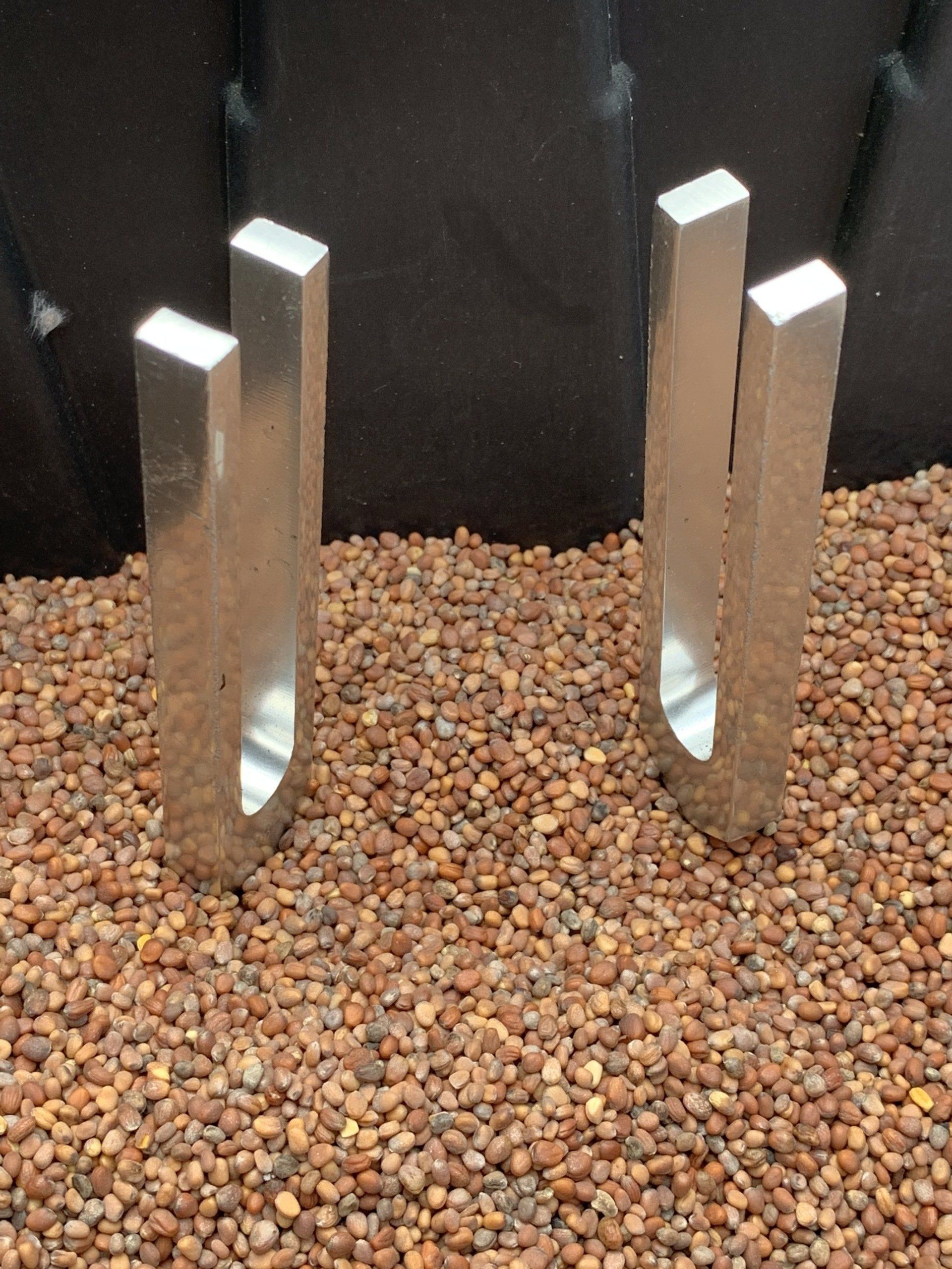 Two silver tuning forks standing on small brown pebbles against a black background.