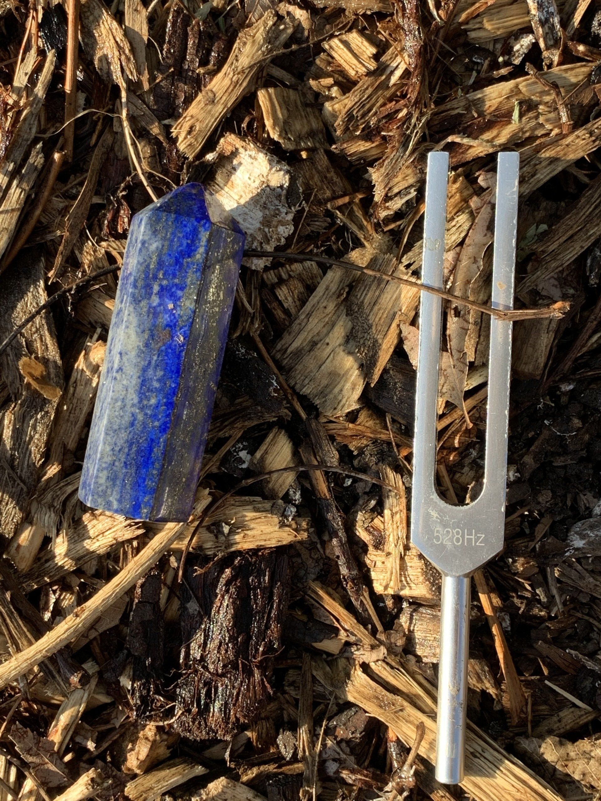 Blue crystal and silver tuning fork on wood chips.