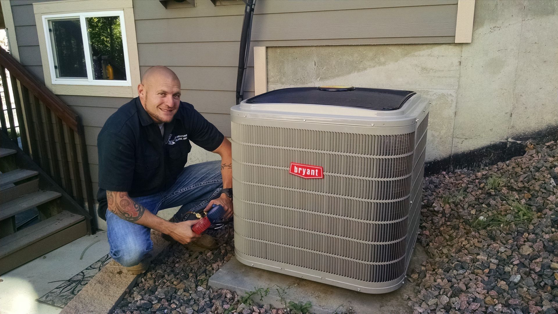 Man kneeling next to an AC unit, using a tool. Outdoors, next to a building and stairs.