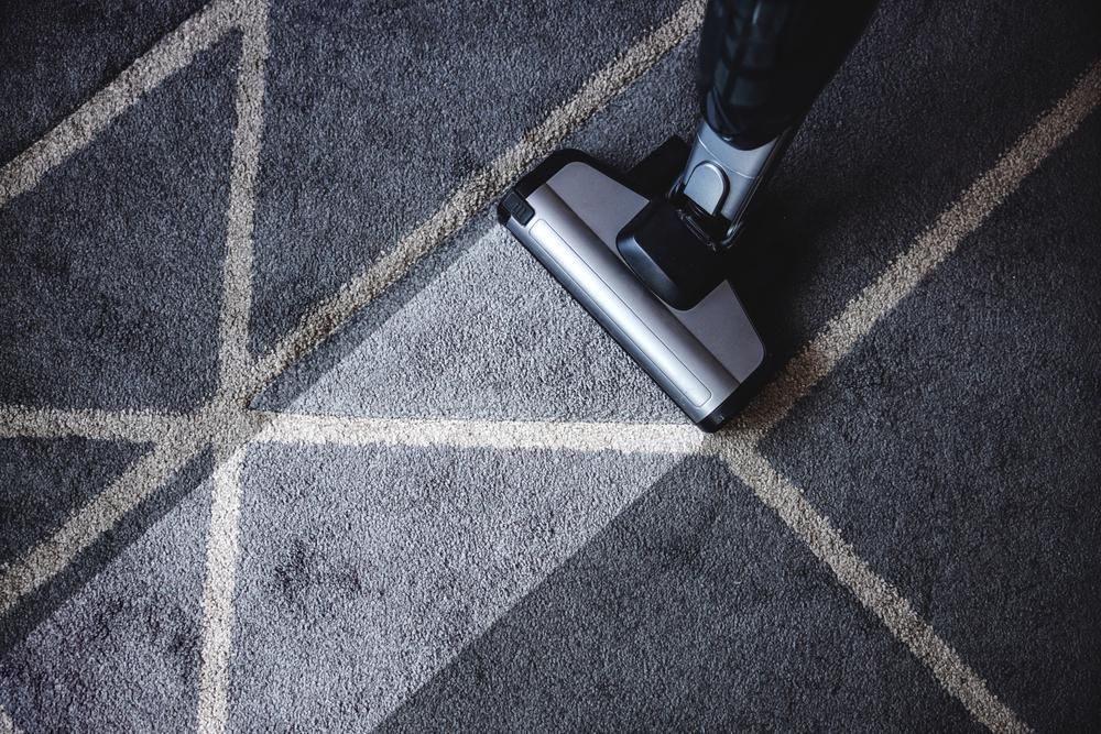 A Person is Using a Vacuum Cleaner to Clean a Carpet — Great Lakes Carpet Cleaning & Restoration In Taree, NSW