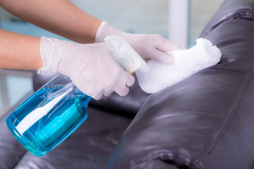 A Person is Cleaning a Leather Couch With a Spray Bottle — Great Lakes Carpet Cleaning & Restoration In Hallidays Point, NSW