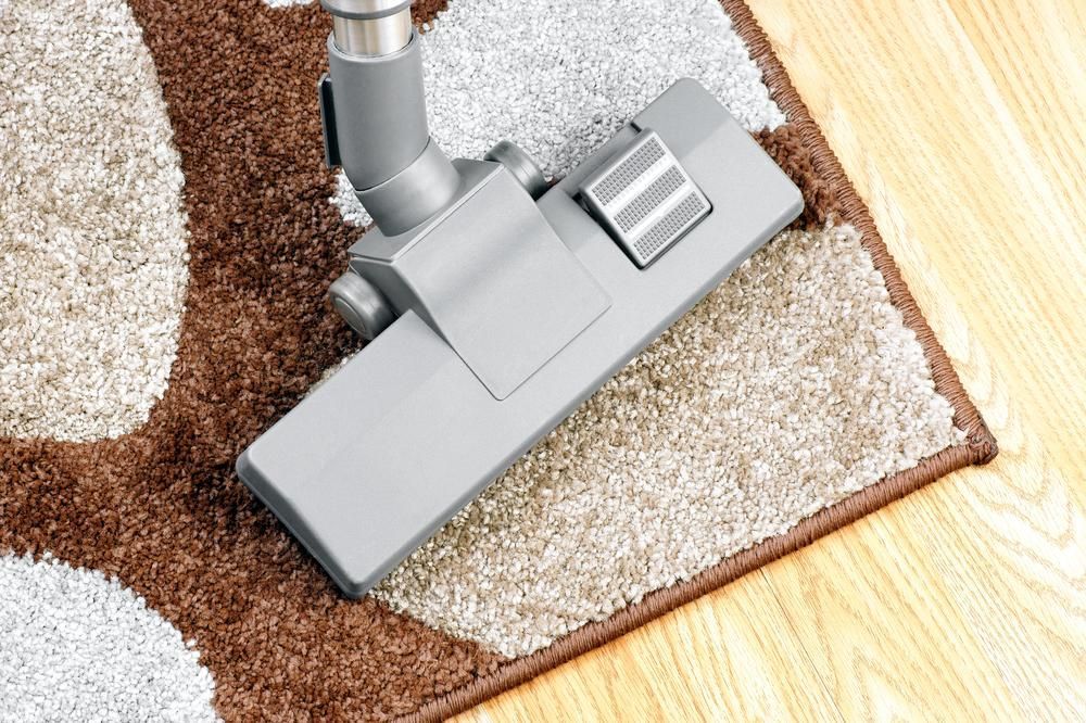 A Vacuum Cleaner is Cleaning a Rug on a Wooden Floor — Great Lakes Carpet Cleaning & Restoration In Harrington, NSW