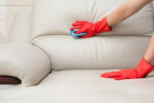 A Person Wearing Red Gloves is Cleaning a White Leather Couch — Great Lakes Carpet Cleaning & Restoration In Hallidays Point, NSW