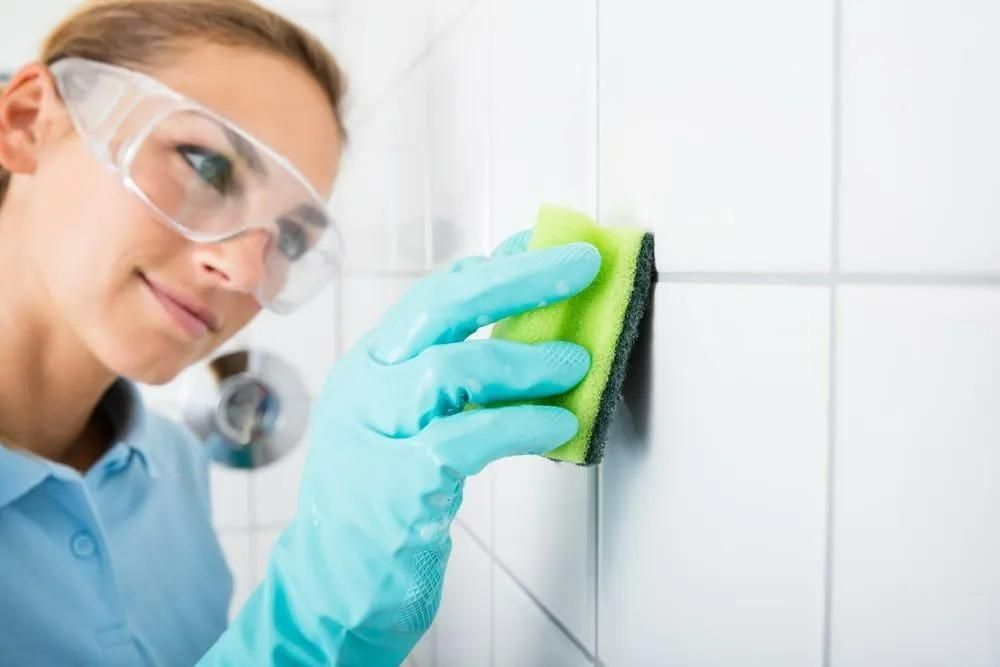 A Woman is Cleaning a Tile Wall With a Sponge — Great Lakes Carpet Cleaning & Restoration In Hallidays Point, NSW