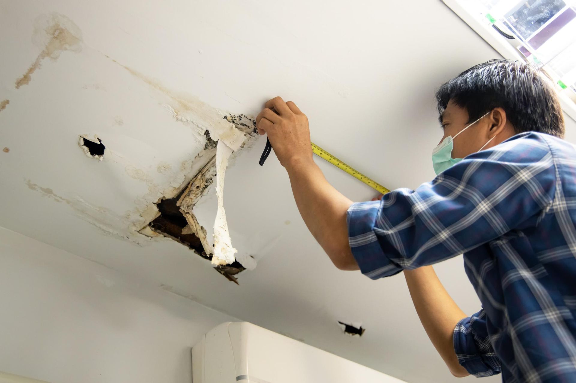A Man is Measuring a Ceiling With a Tape Measure — Great Lakes Carpet Cleaning & Restoration In Port Macquarie, NSW