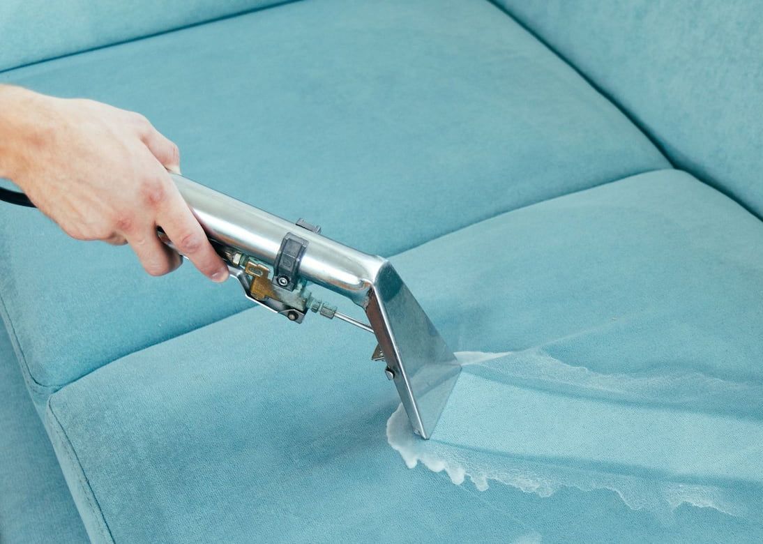 A Person is Cleaning a Blue Couch With a Vacuum Cleaner — Great Lakes Carpet Cleaning & Restoration In Hallidays Point, NSW