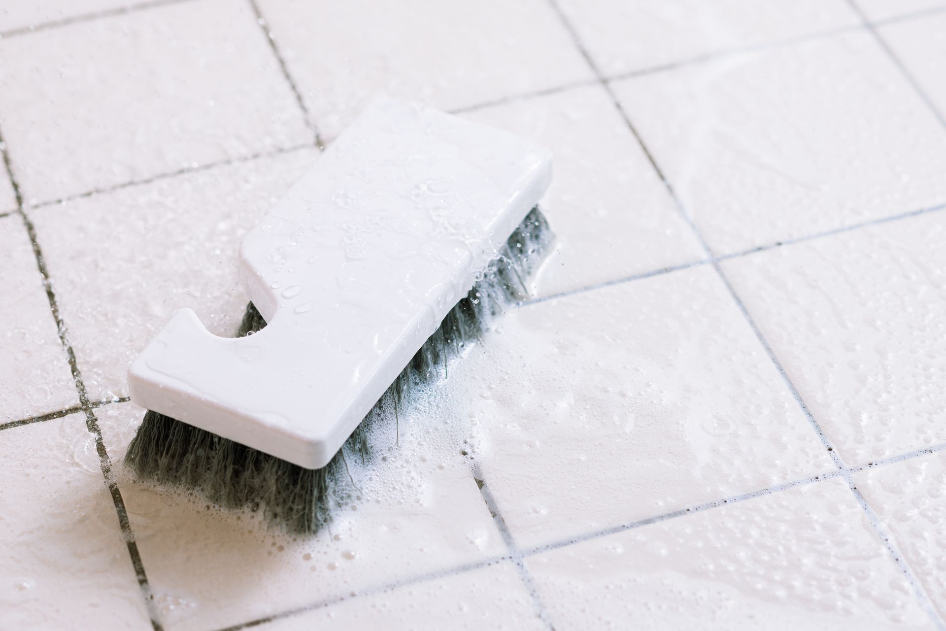 A Brush is Sitting on a Tiled Floor — Great Lakes Carpet Cleaning & Restoration In Hallidays Point, NSW